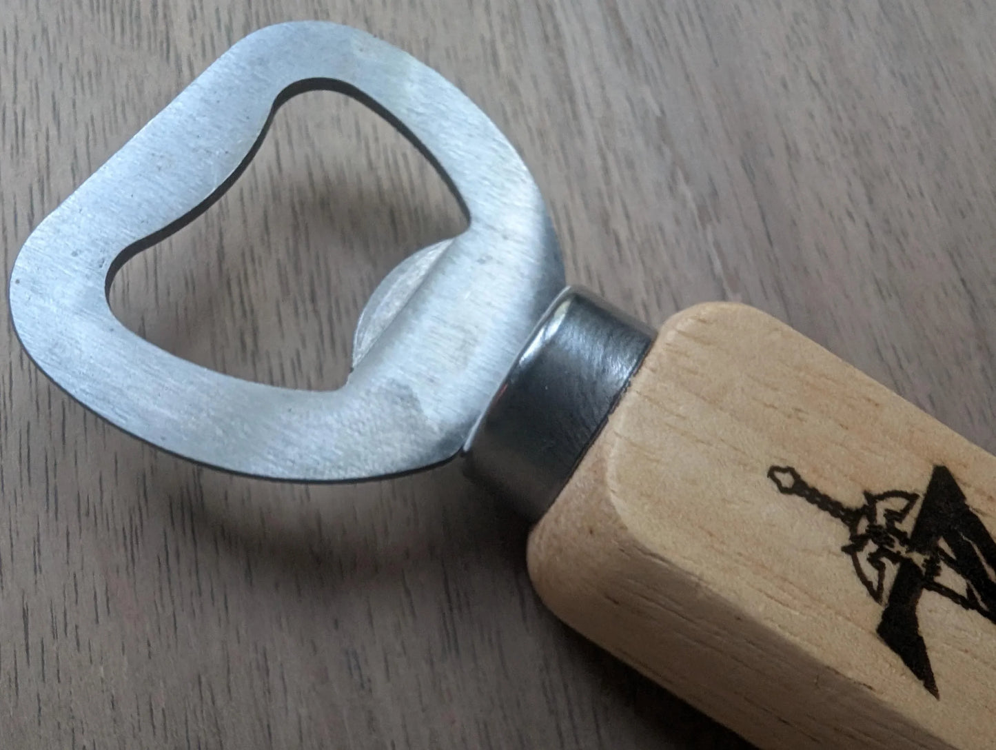 Metal bottle opener with wooden handle featuring a sword graphic, on wood surface