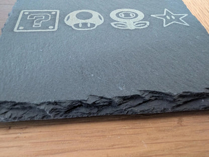 Engraved slate coaster with video game icons on a wooden surface
