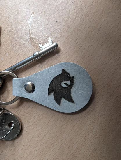 Custom engraved leather keychain with wolf silhouette next to metal keys on wooden surface