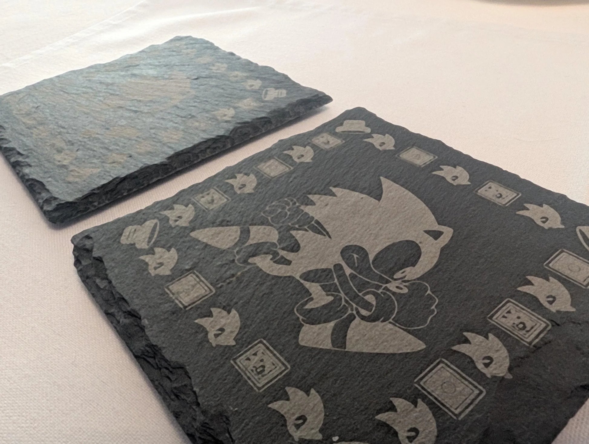 Engraved slate coasters featuring a cartoon character and decorative border on a table