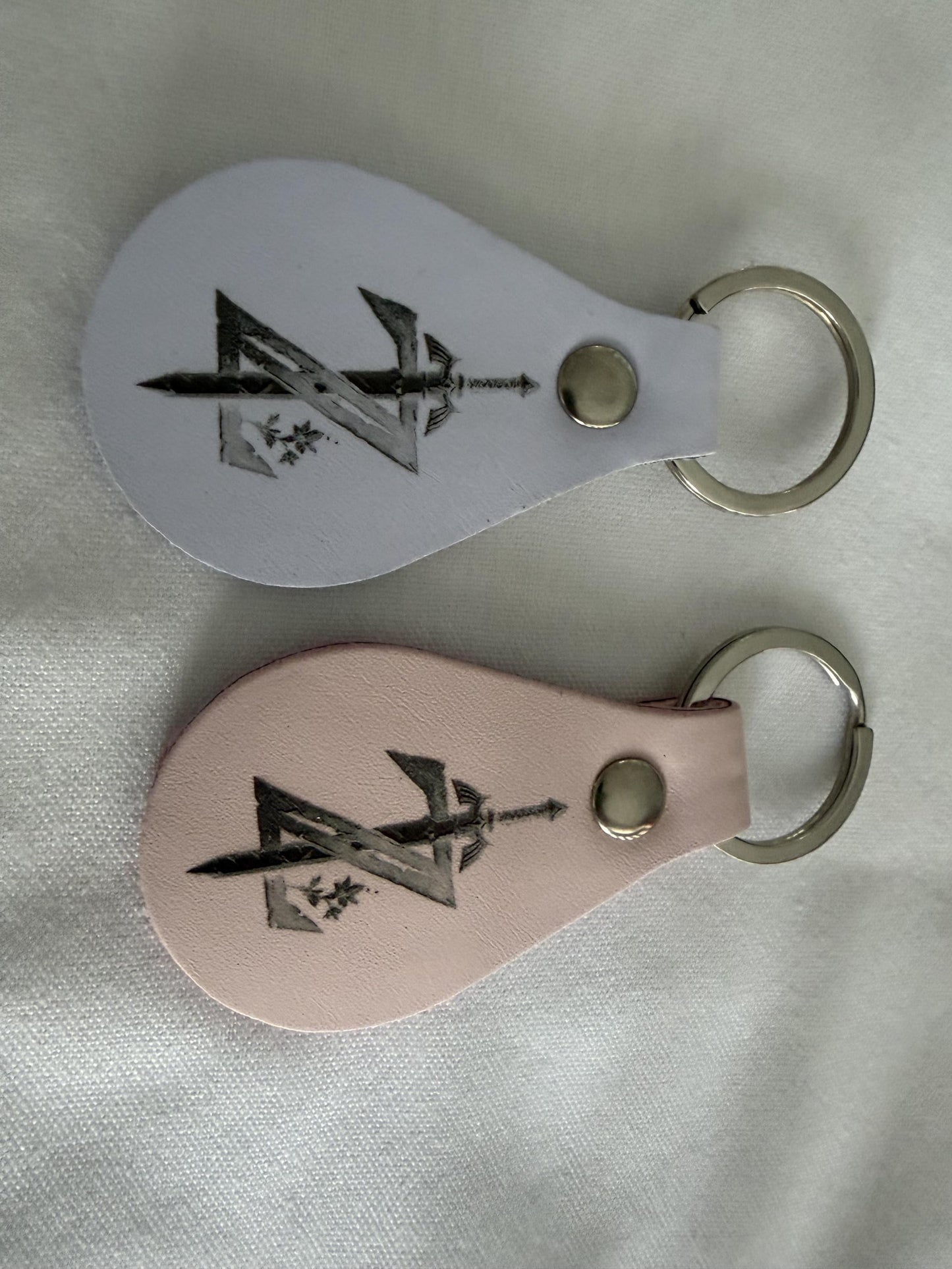 Custom engraved leather keychains with sword and arrow design on white fabric background