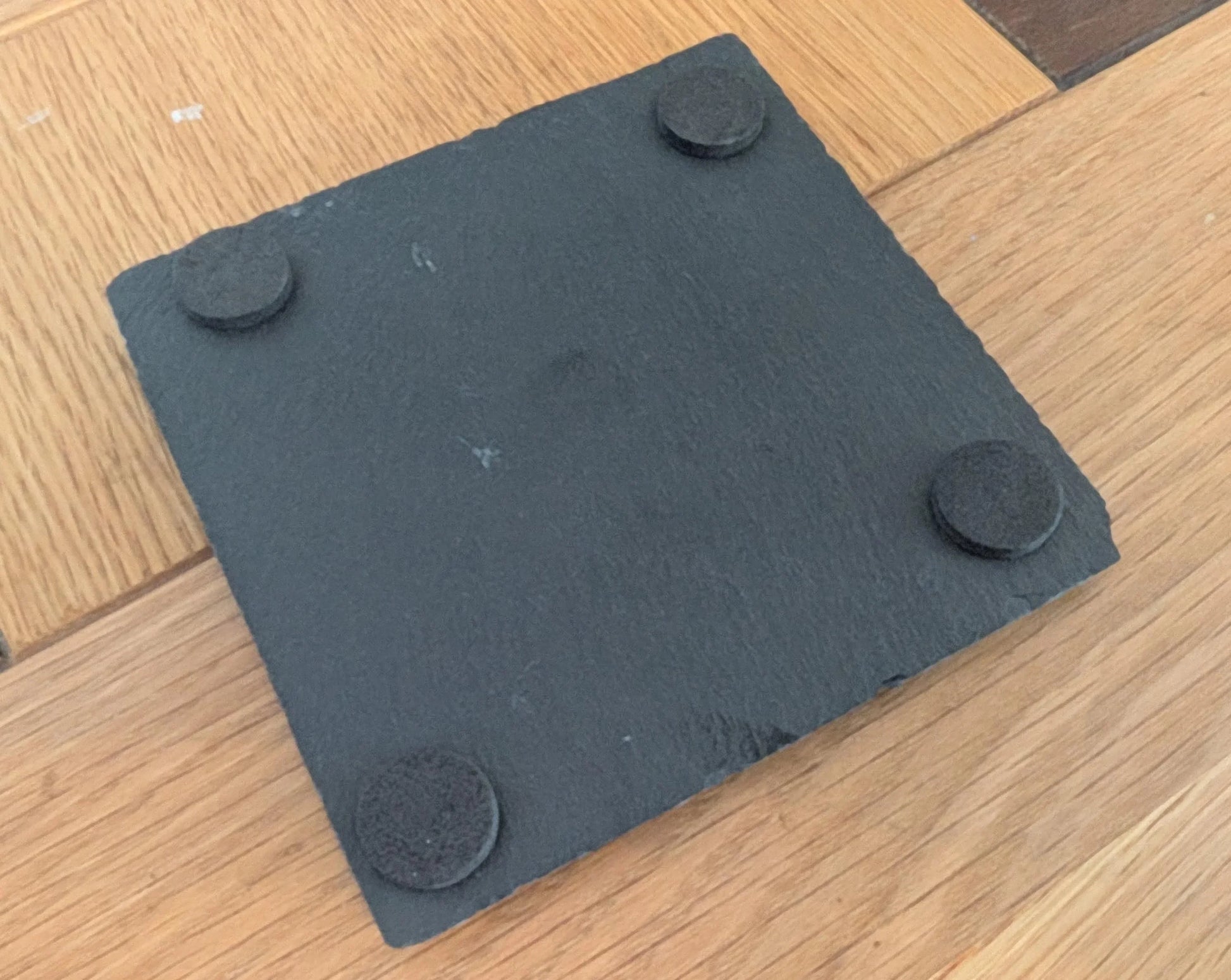 Square black slate coaster with felt pads on wooden floor