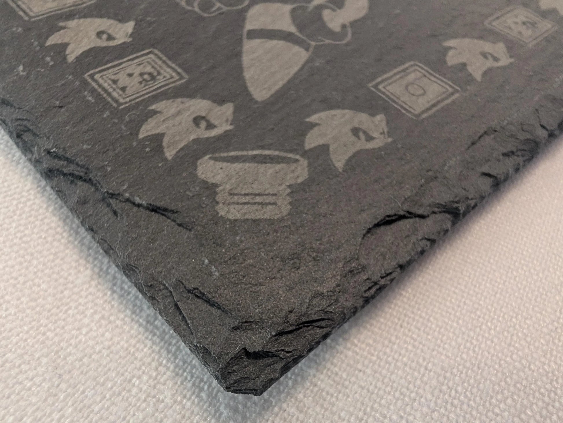 Engraved black slate coaster with video game inspired motifs on a white surface