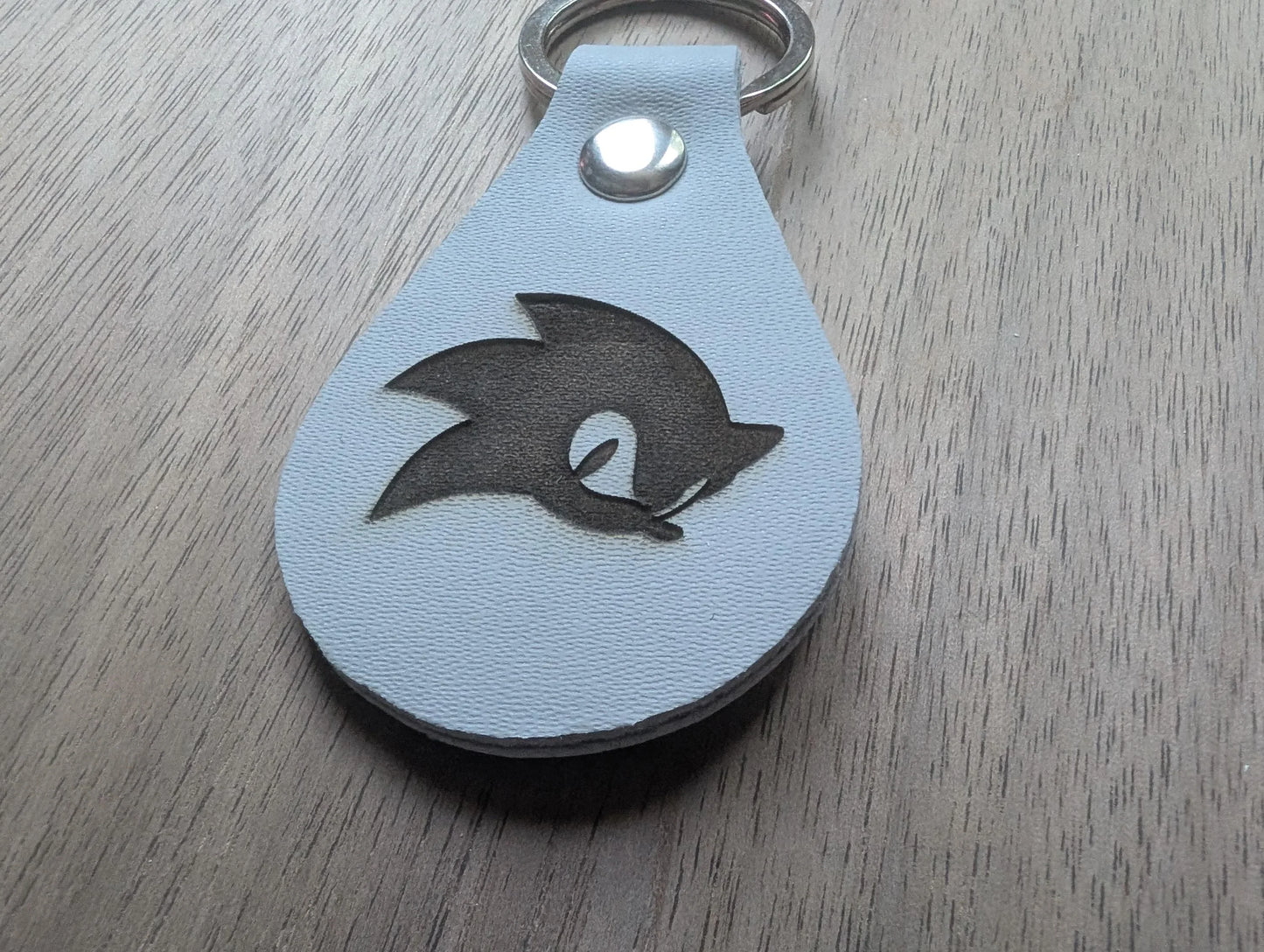 Custom engraved white leather keychain with black silhouette design on wood surface