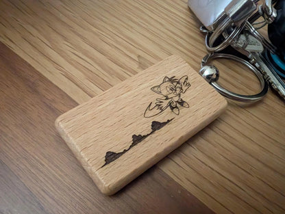 Custom engraved wooden keychain with cartoon character and mountain design, on keyring