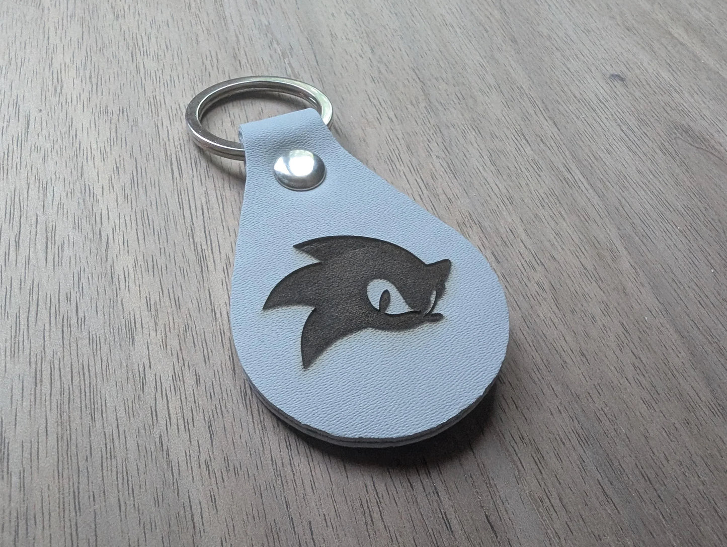 Custom engraved leather keychain with a cartoon hedgehog face on wood background