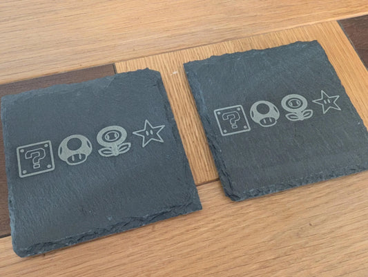 Custom engraved slate coasters with video game icons on a wooden table