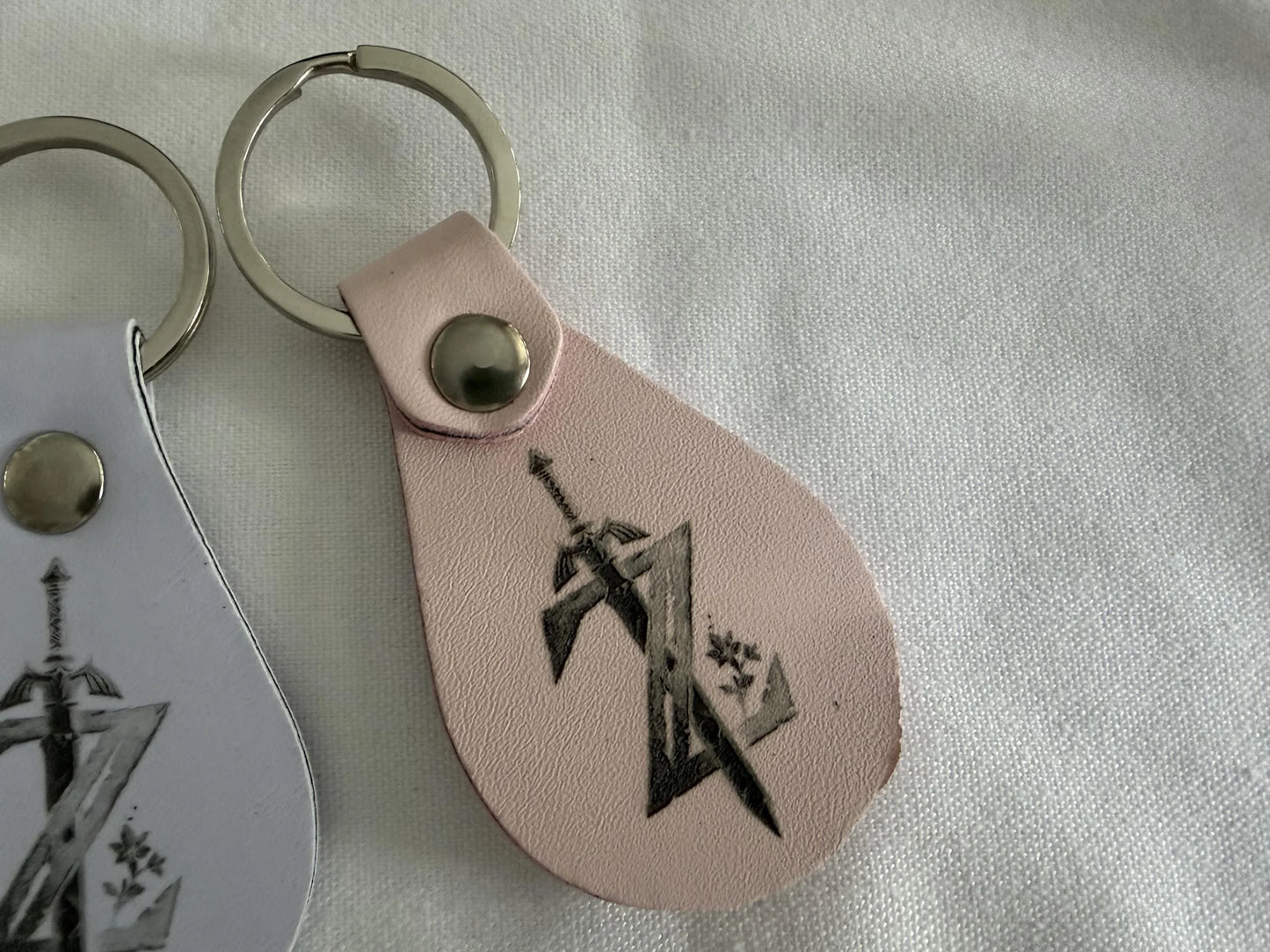 Custom leather keychain with engraved sword and geometric design on light pink background