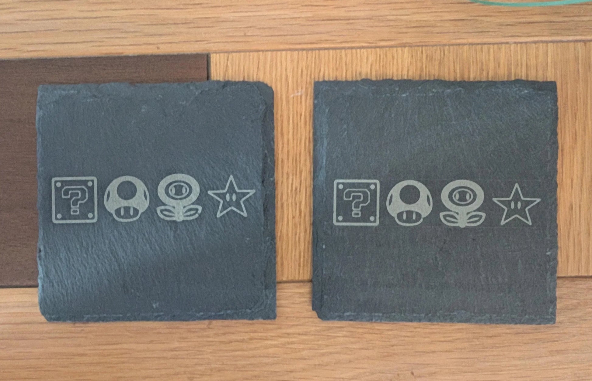 Custom engraved slate coasters with retro video game icons on wood surface