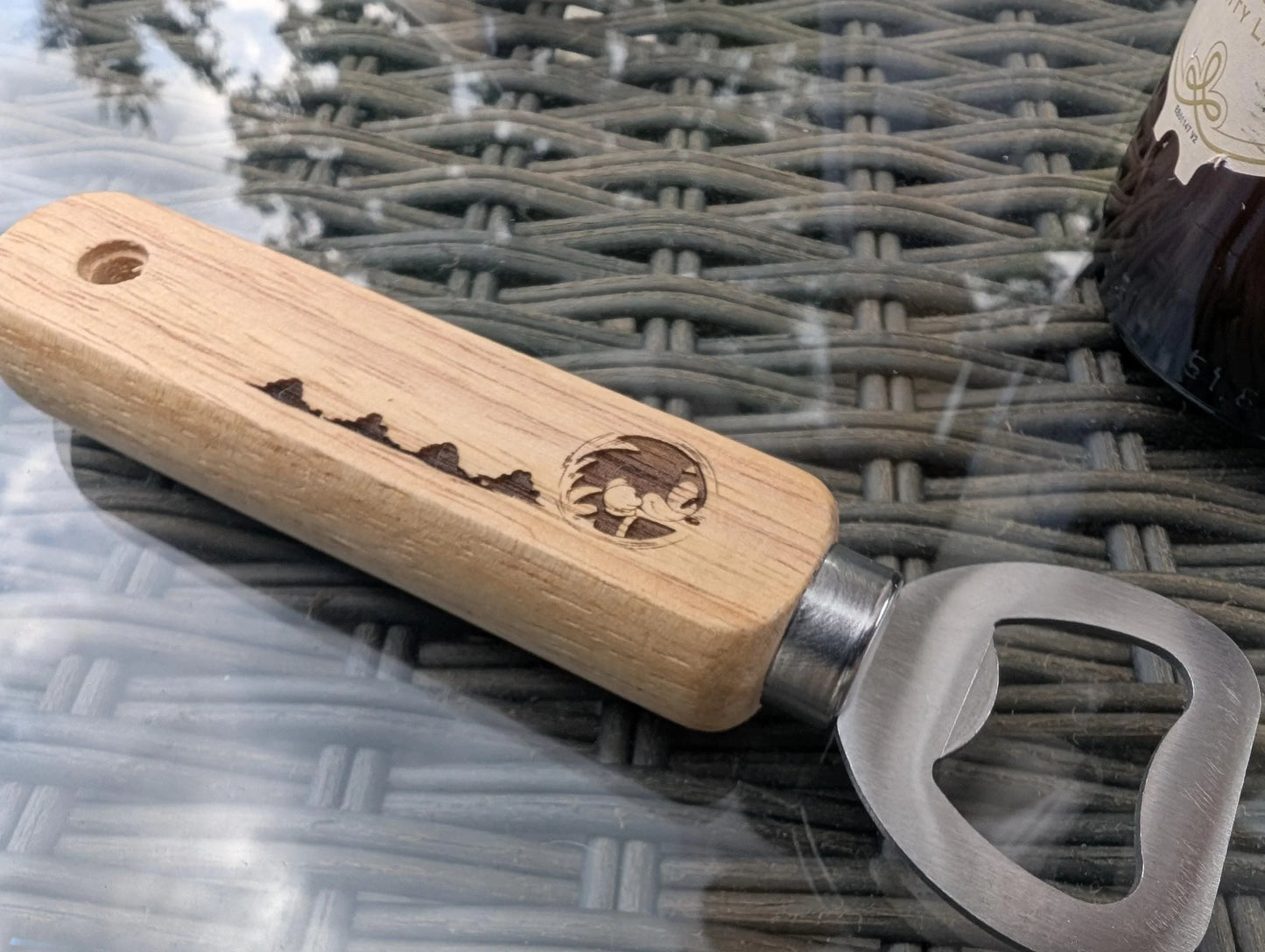 Custom wood bottle opener with engraved mountain scene on wicker table