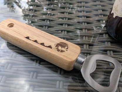 Custom wood bottle opener with engraved mountain scene on wicker table