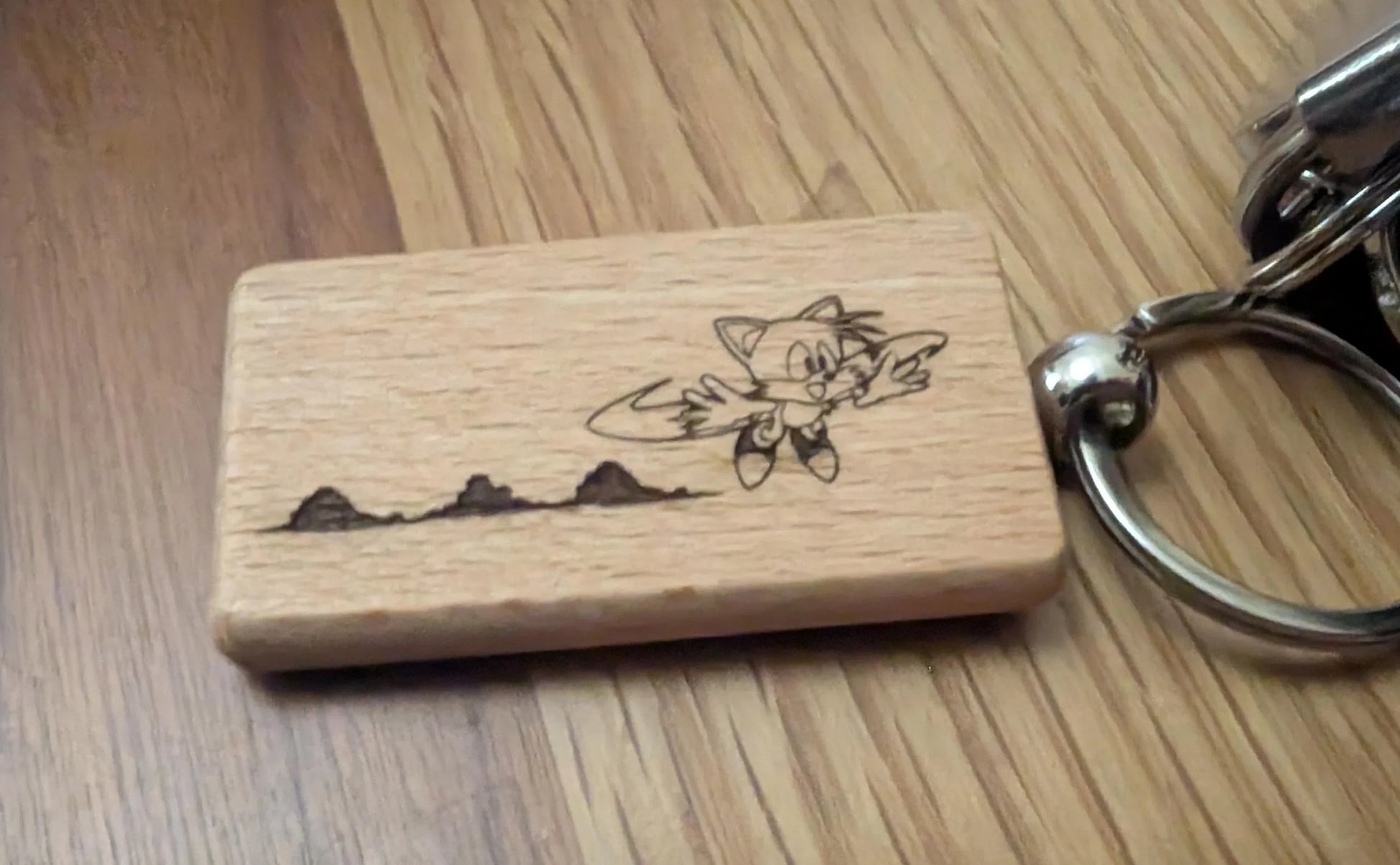 Laser engraved wood keychain with cartoon fox design and metal ring on wood surface