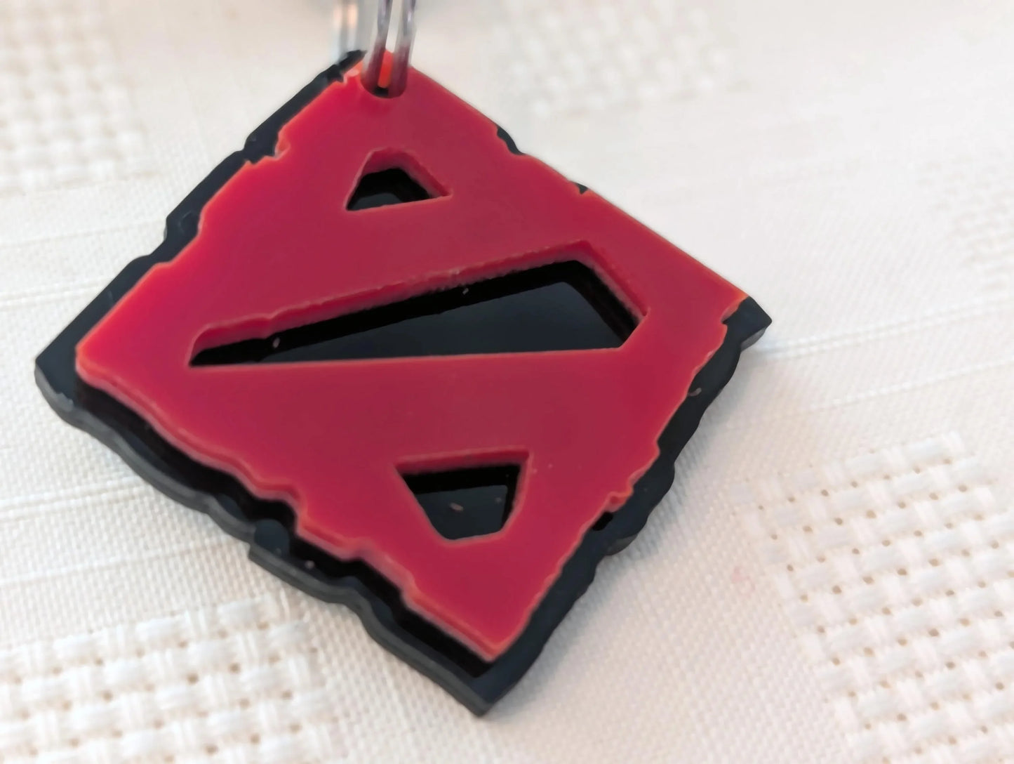 Red and black custom acrylic keychain with geometric cutout design on white textured surface