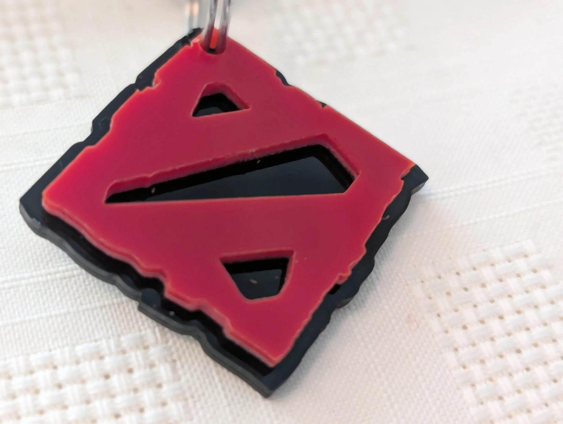 Red and black custom acrylic keychain with geometric cutout design on white textured surface