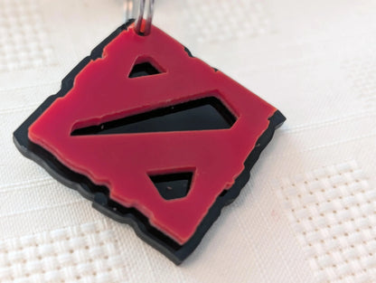 Red and black custom acrylic keychain with geometric cutout design on white textured surface