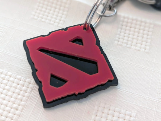 Red and black acrylic keychain with geometric cutout design on textured white surface