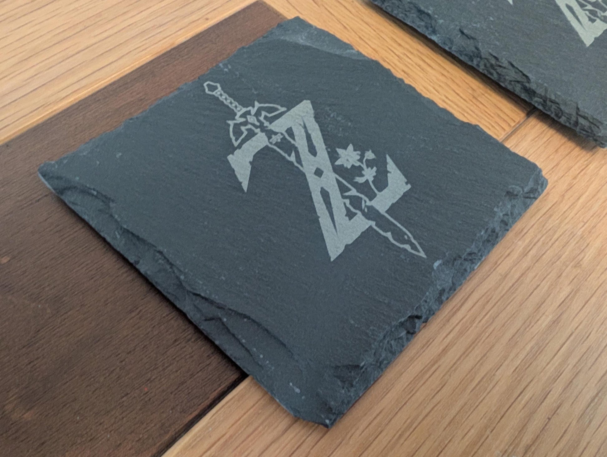 Custom engraved slate coaster with sword and floral design on wood surface