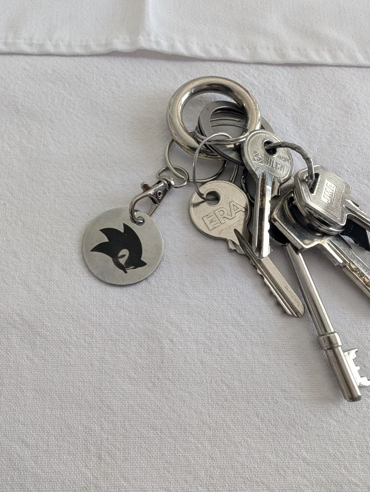 Custom metal keychain with engraved animal silhouette and assorted keys on white fabric