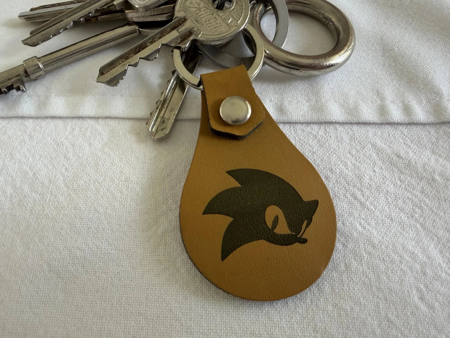 Brown leather keychain with graphic design attached to silver keys on white fabric
