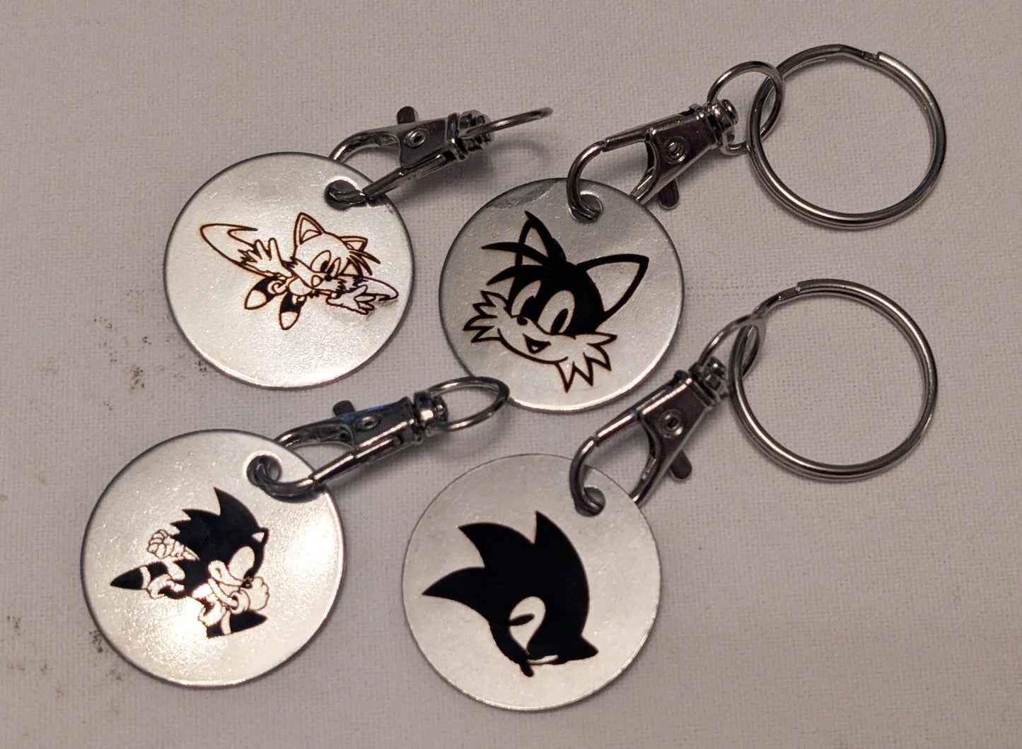 Set of four custom engraved metal keychains with cartoon character designs on round silver tags
