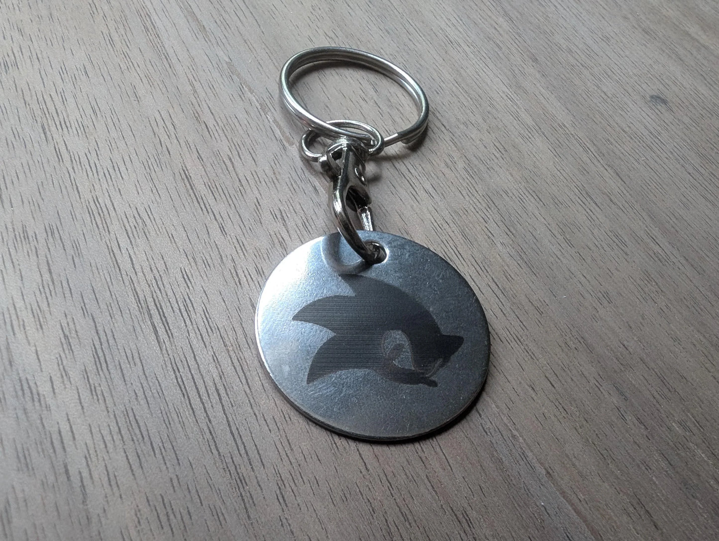 Round custom metal keychain with engraved design on wood surface