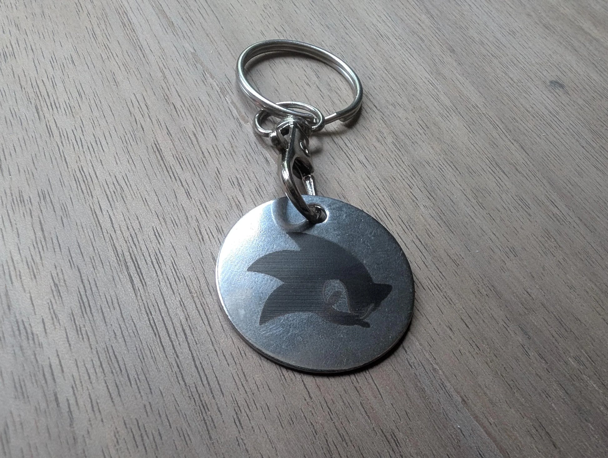 Round custom metal keychain with engraved design on wood surface