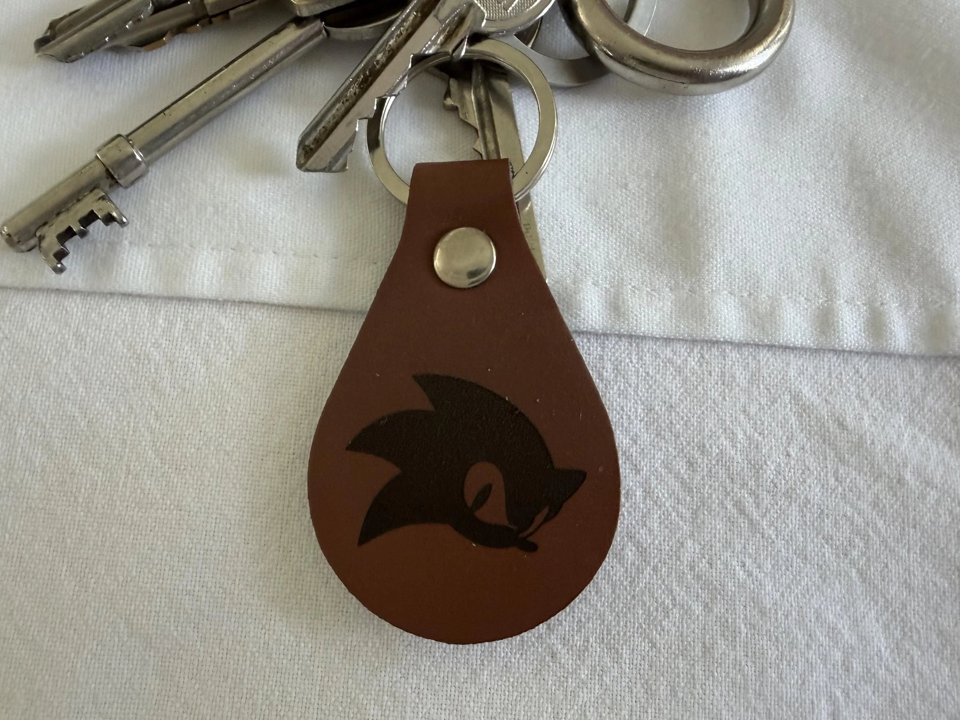 Brown leather keychain with engraved design attached to silver keys on white fabric