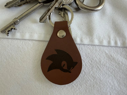 Brown leather keychain with engraved design attached to silver keys on white fabric