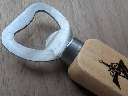 Metal bottle opener with wooden handle featuring a sword graphic, on wood surface