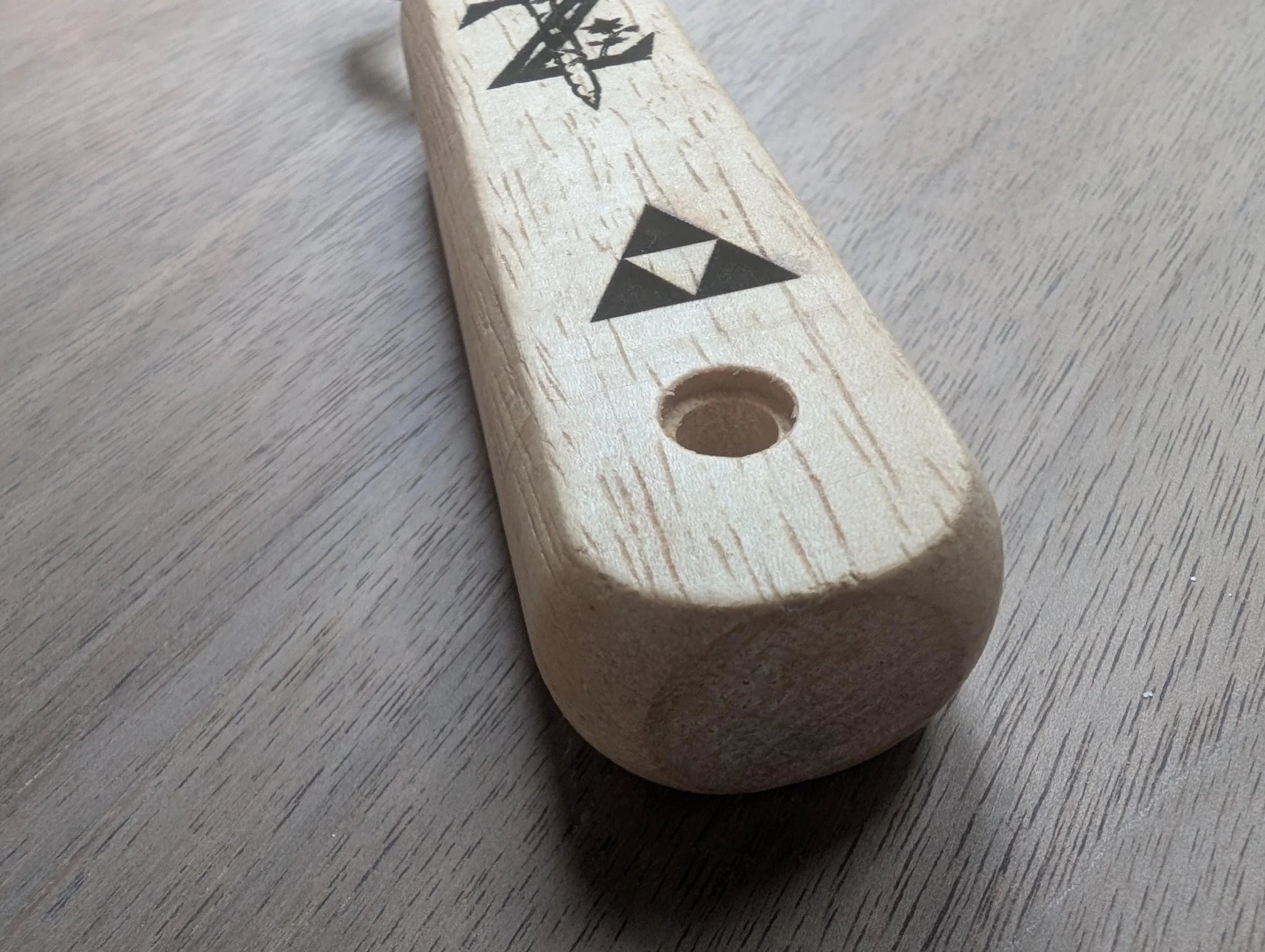 Wooden handle with laser-engraved geometric symbols on light wood surface