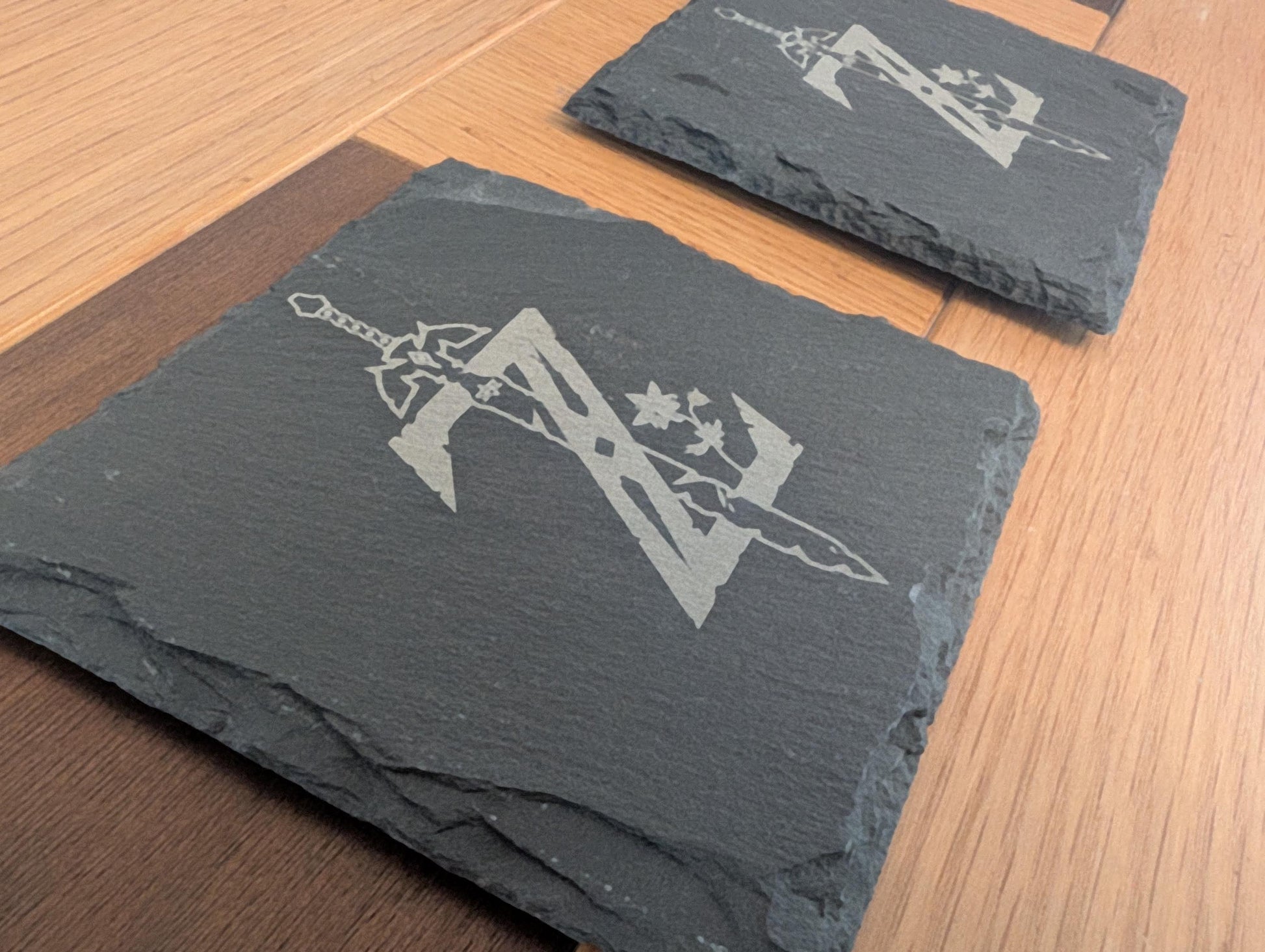 Engraved slate coasters with sword and letter design on wooden surface