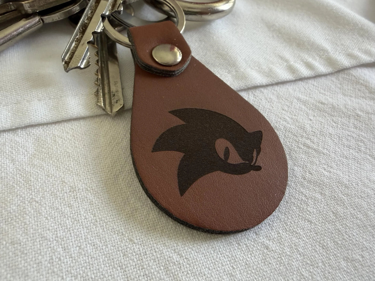 Custom brown leather keychain with black graphic, attached to metal keys on fabric