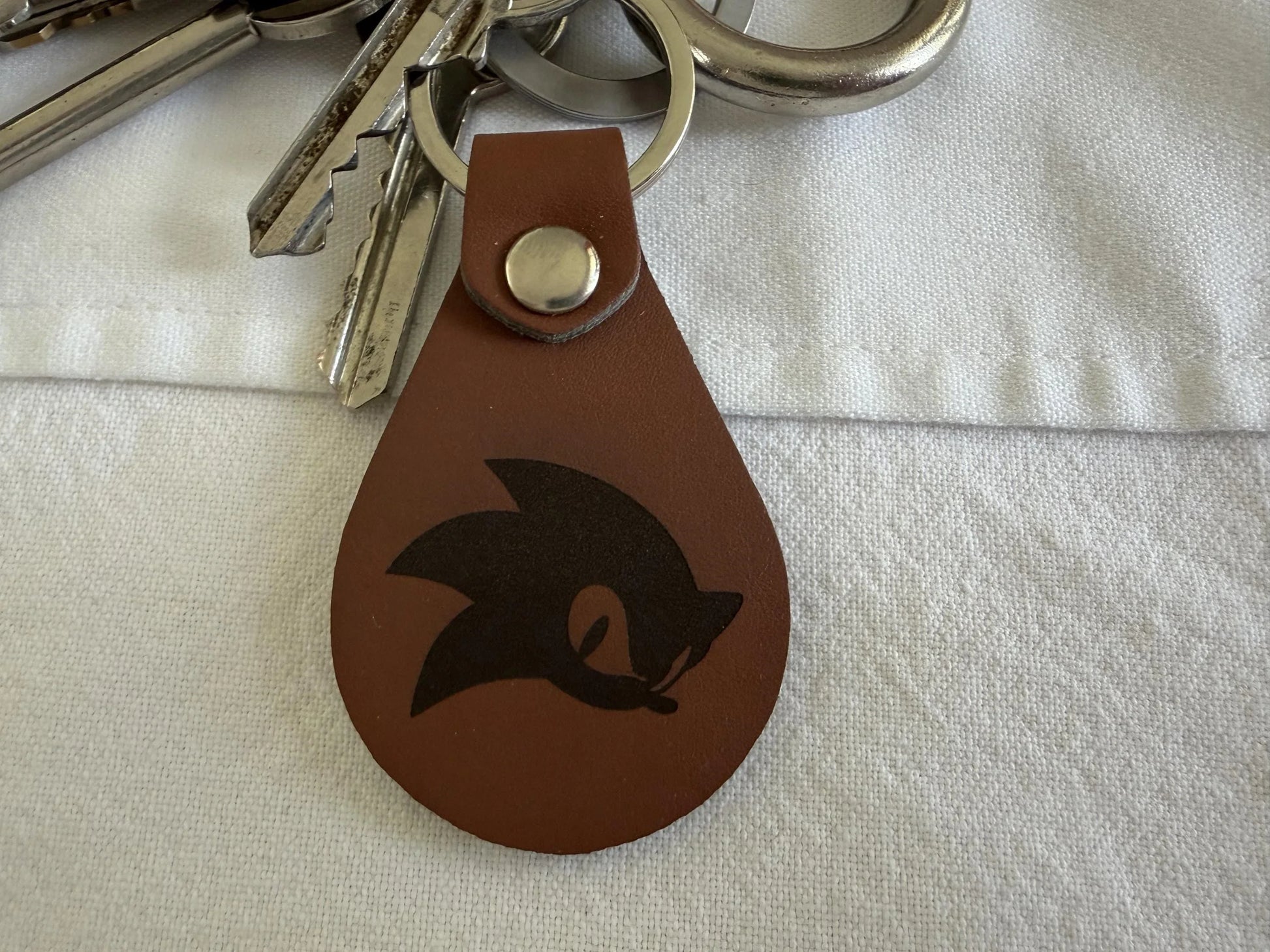 Brown leather keychain with engraved graphic, metal rivet, attached to silver keys
