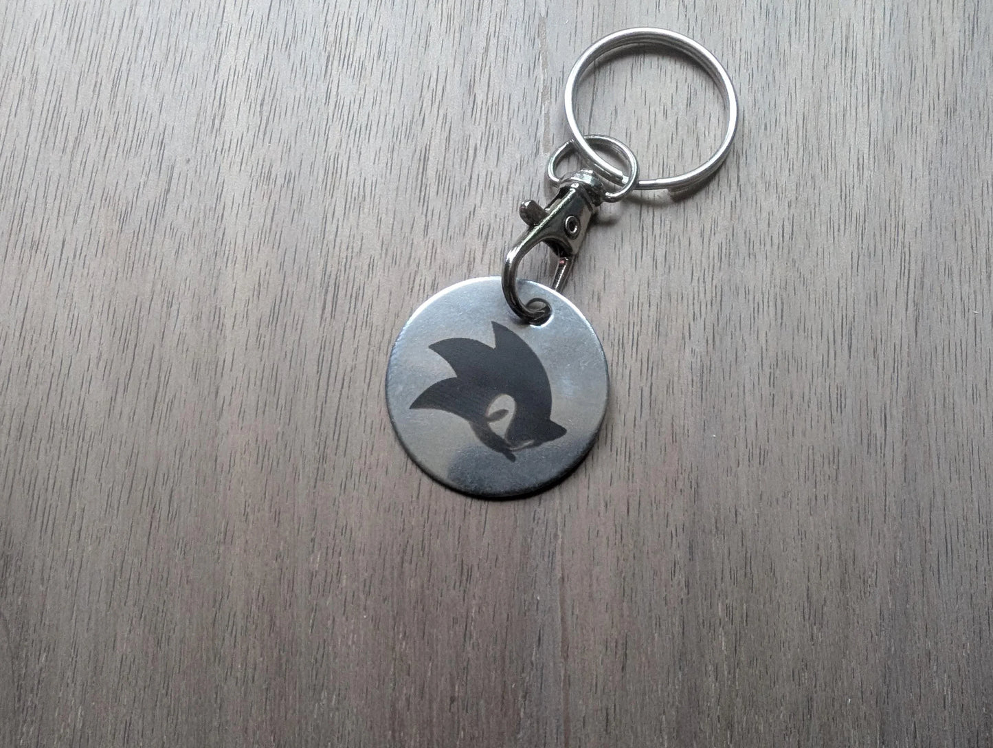 Round metal keychain with engraved abstract design on wood surface