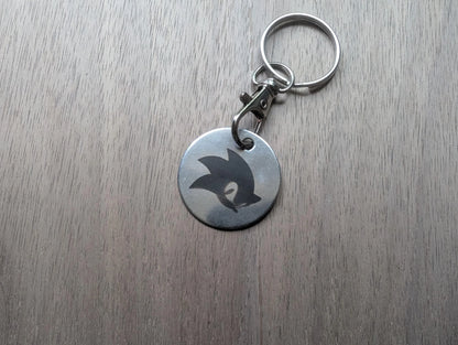 Round metal keychain with engraved abstract design on wood surface