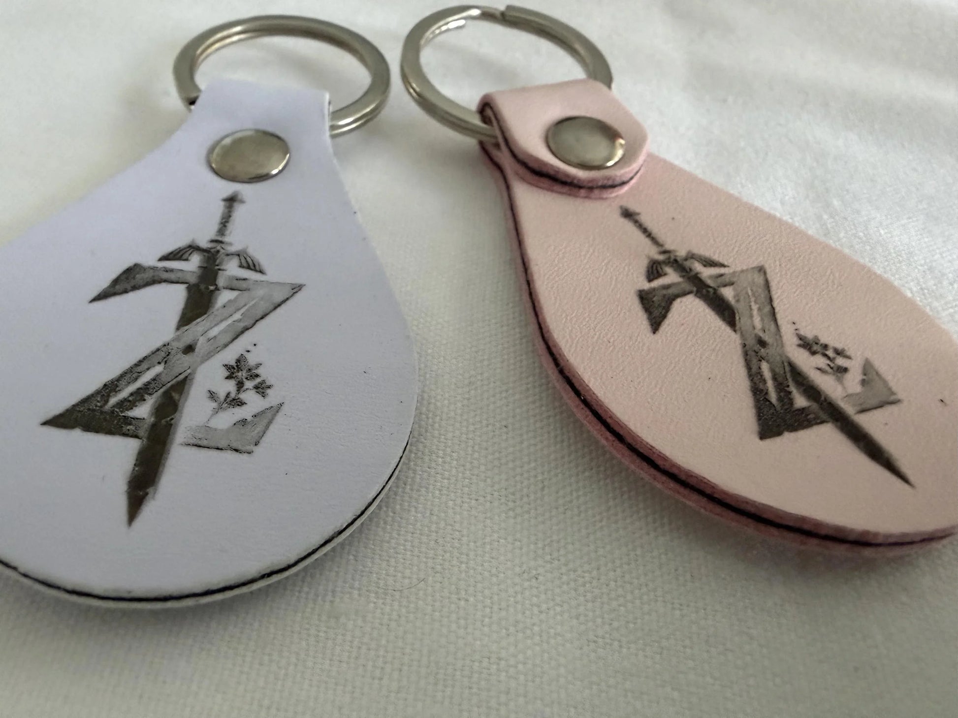 Custom leather keychains with engraved sword and symbol design, metal key rings, on fabric