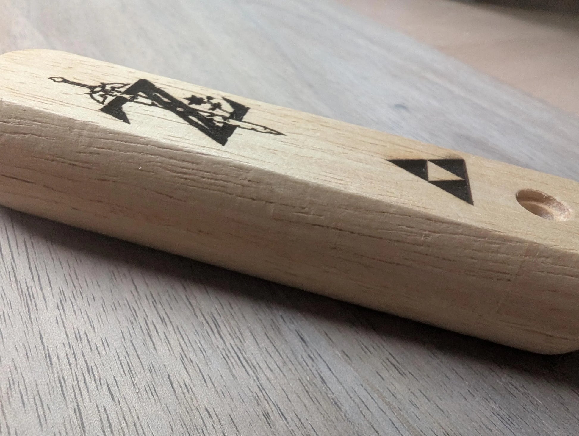 Wooden handle with engraved geometric and sword designs on a light wood surface