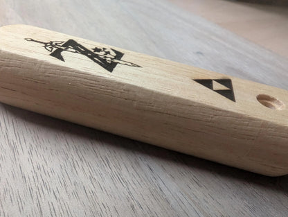 Wooden handle with engraved geometric and sword designs on a light wood surface