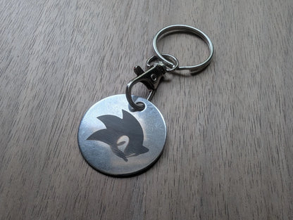 Round metal keychain with engraved stylized silhouette on wooden surface