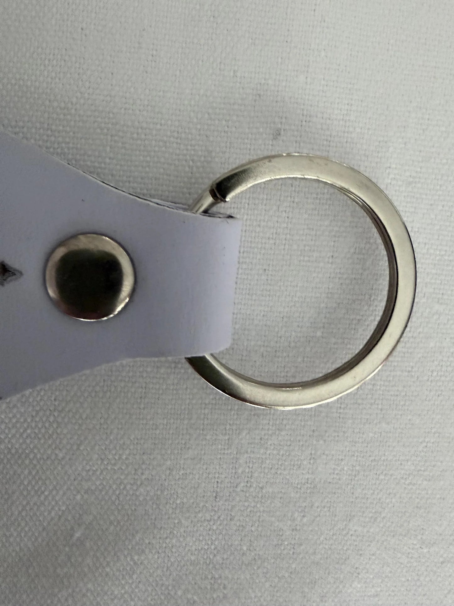 Close-up of a metal keyring with a white leather strap on a fabric surface
