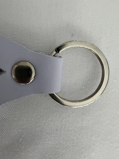 Close-up of a metal keyring with a white leather strap on a fabric surface