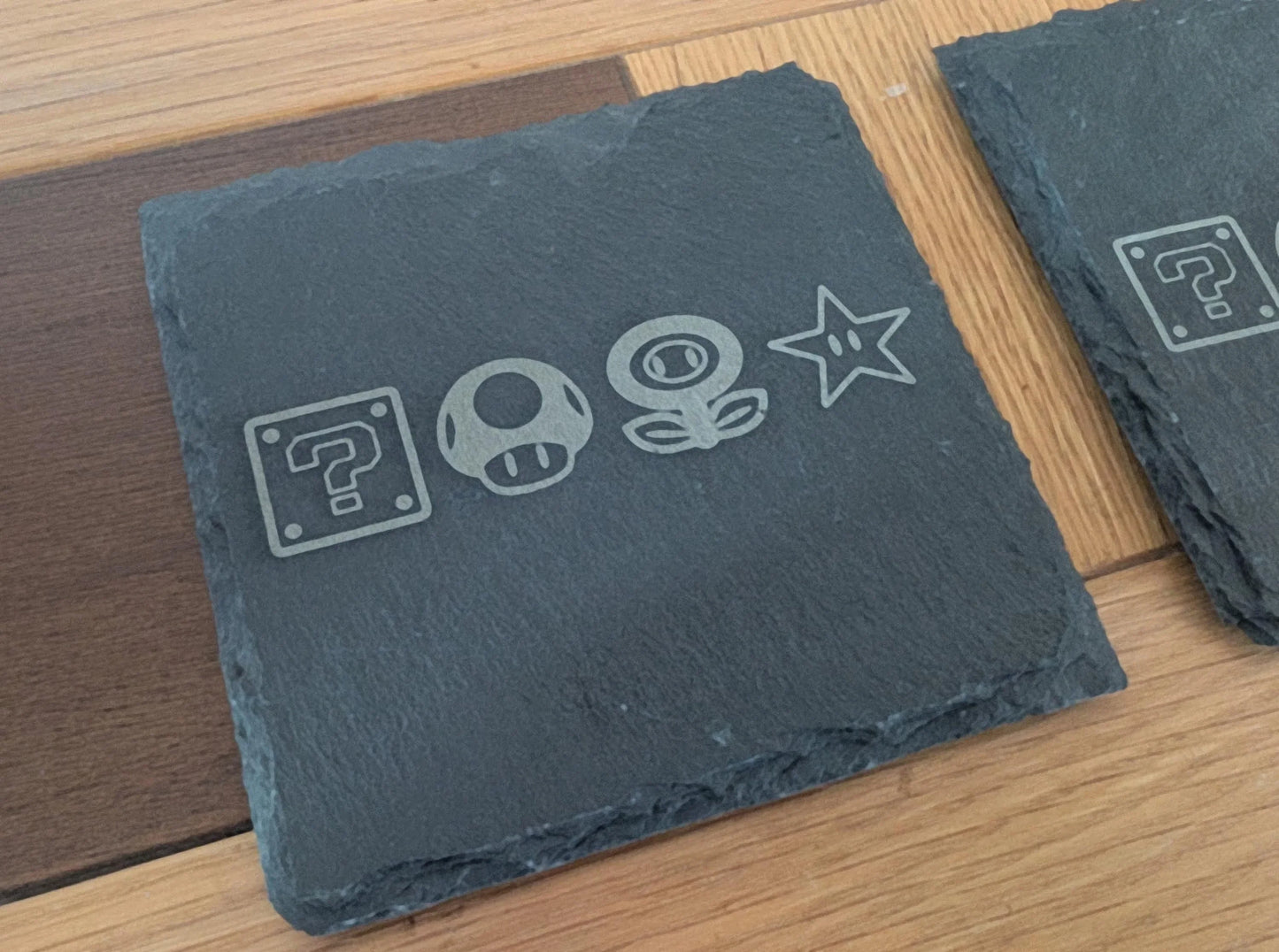 Custom engraved slate coaster with video game themed icons on wood table