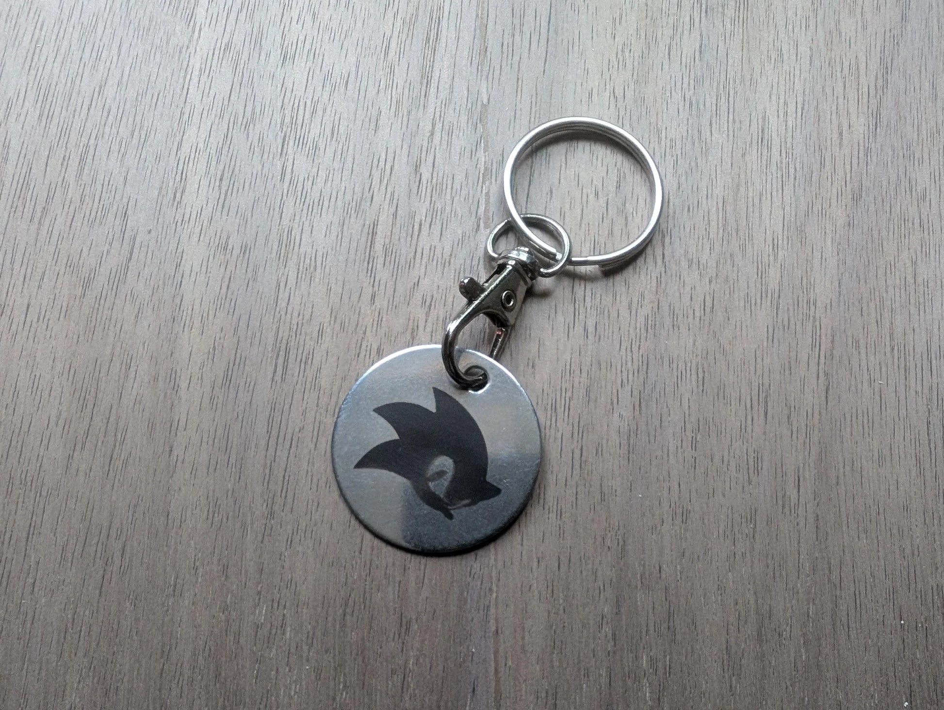 Round metal keychain with engraved silhouette on wood surface