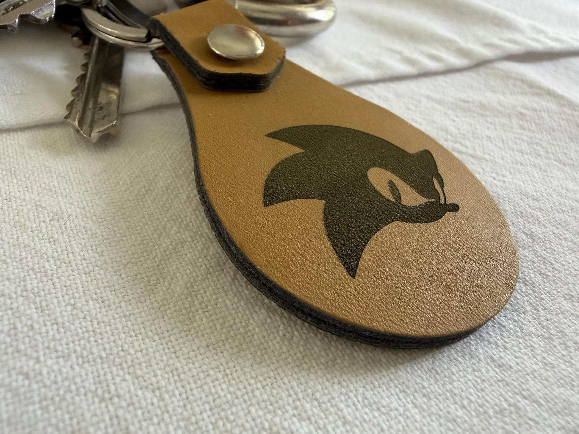 Brown leather keychain with black cartoon graphic, metal keyring, and keys on white fabric