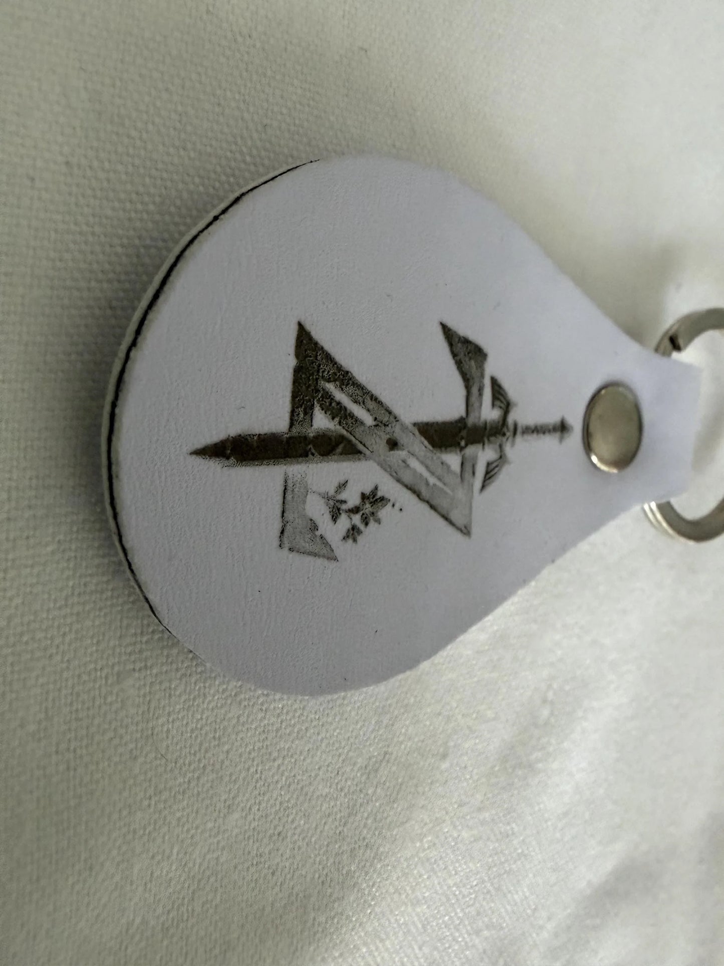 Custom white leather keychain with engraved sword and geometric design on metal ring
