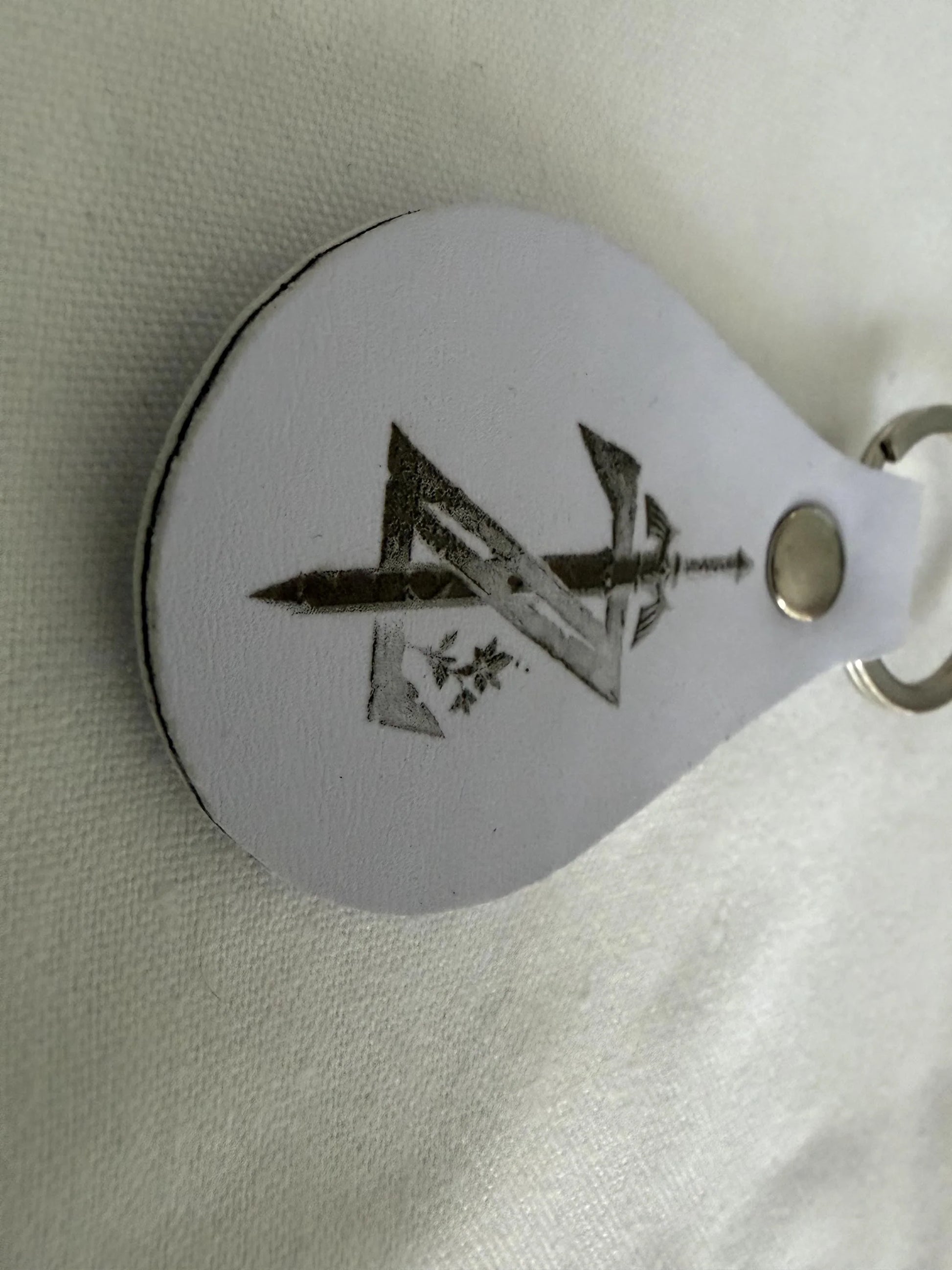Custom white leather keychain with engraved sword and geometric design on metal ring