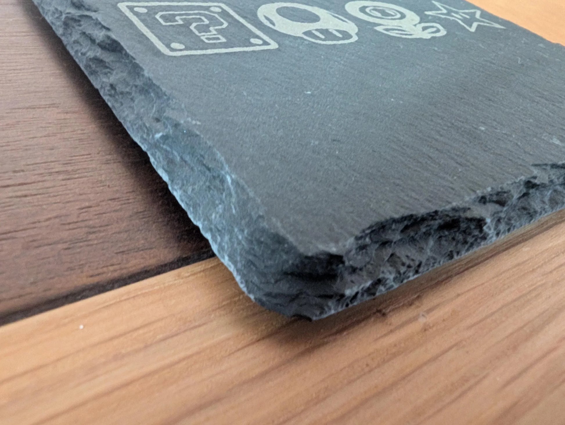 Close-up of engraved slate sign with rough edge on wood surface, custom decor material.