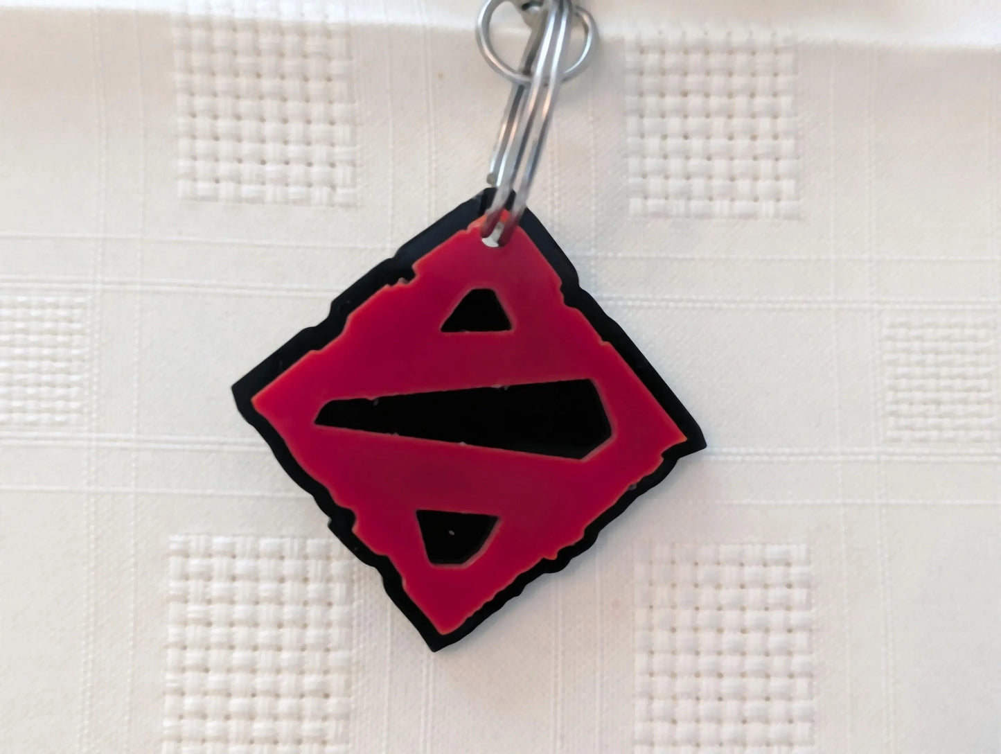 Custom acrylic keychain with red and black geometric design on textured surface.