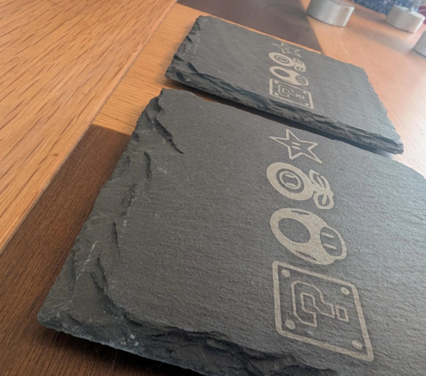 Custom engraved slate coasters with game-inspired icons on a wooden table