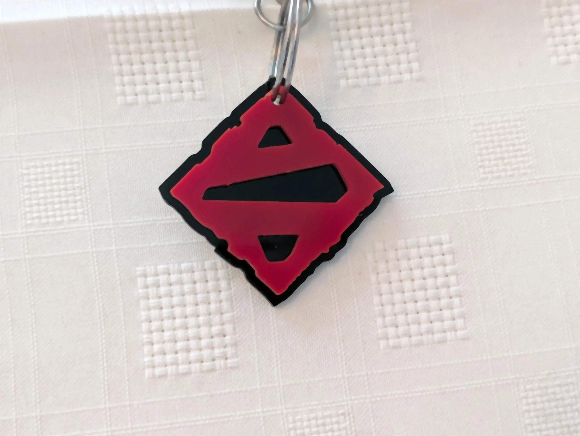 Custom black and red acrylic keychain with geometric cutout design on textured white background